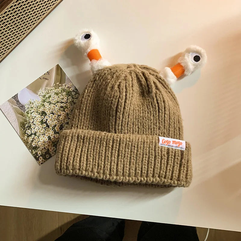 Beige knit beanie with duck-shaped ear flaps on a light surface.