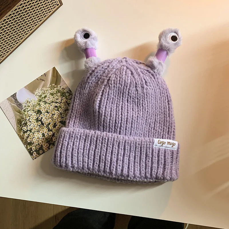 Purple knit beanie with cartoonish duck ears on a light surface.