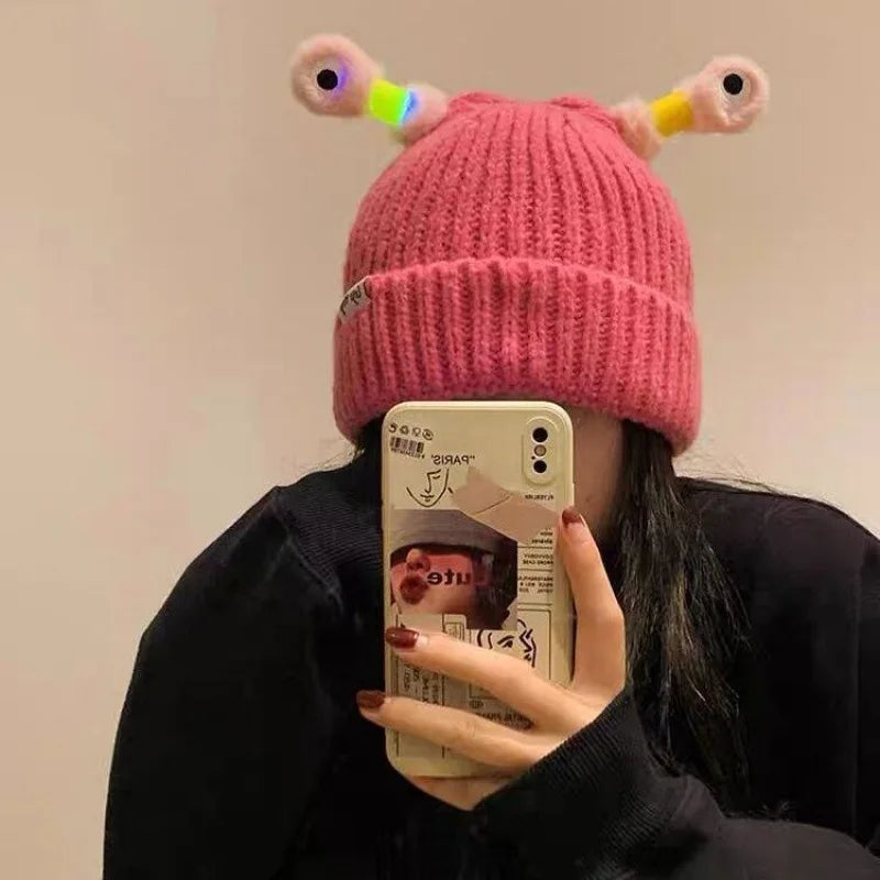 Person wearing a pink knitted hat with colorful accents, holding a phone with a visible brand logo.