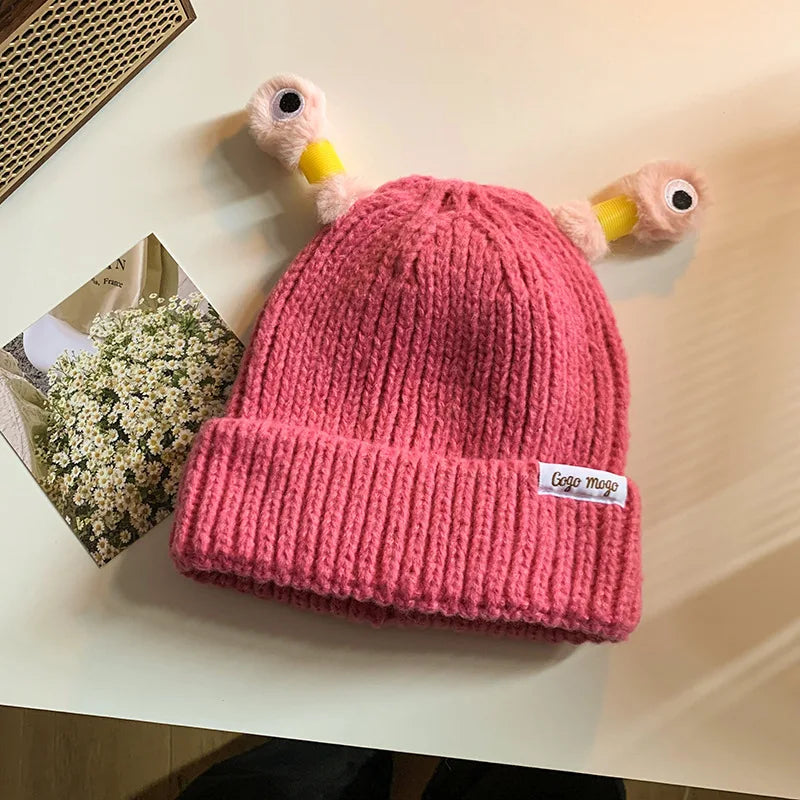 Pink knitted beanie with duck-like ears on a light surface