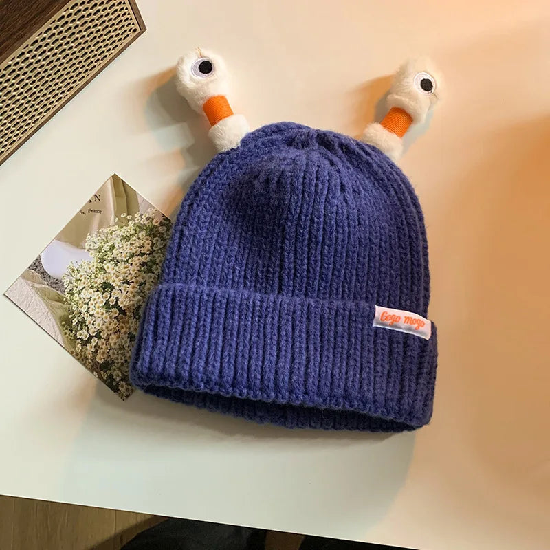 Blue knit beanie with duck head design on a light surface