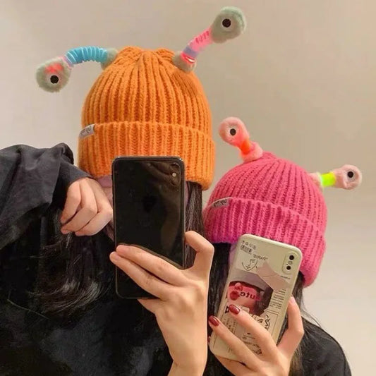 two people wearing colorful beanies with antenna-like decorations with led, taking a mirror selfie.