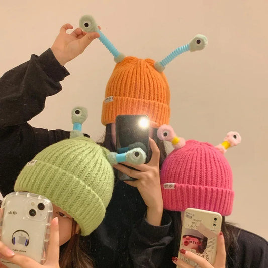 Three people wearing colorful beanies with antenna-like decorations with led, taking a mirror selfie.